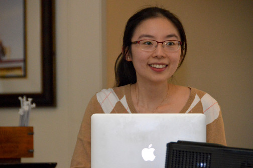 A woman sitting behind a laptop is looking up and grinning.