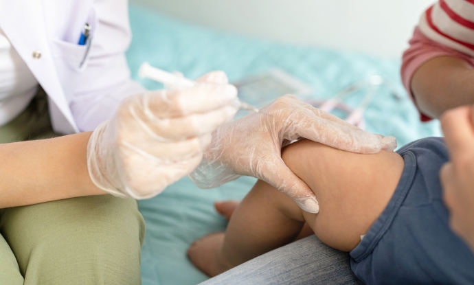 A doctor holding a syringe squeezes the thigh of a baby held by its parent