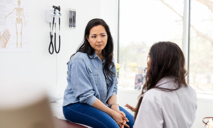 a young person sits and receives bad news from their doctor